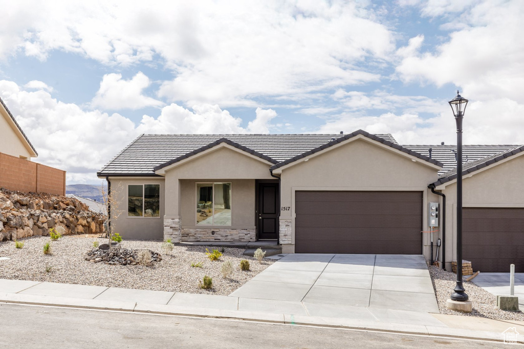 Single story home featuring stucco siding, an attached garage, driveway, a tiled roof, and stone siding