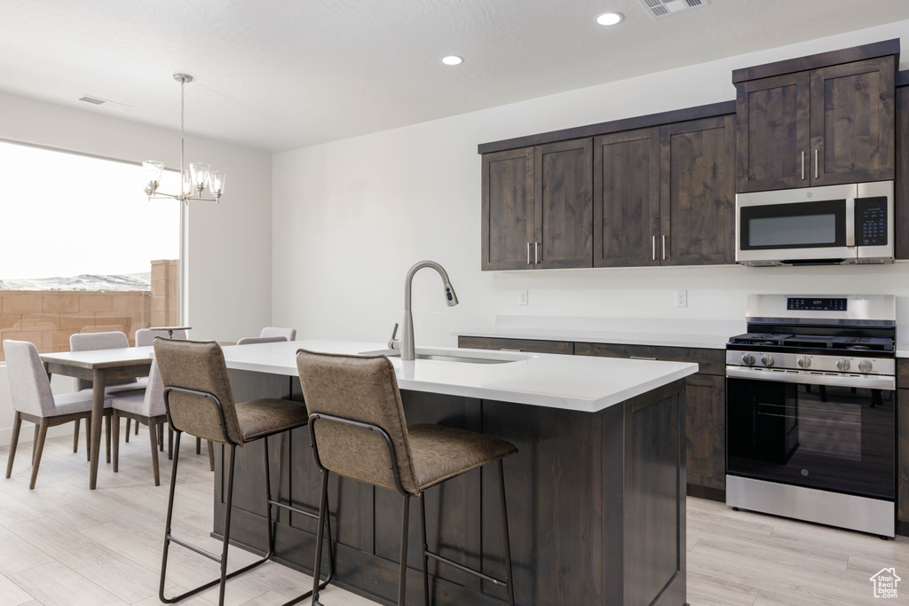 Kitchen with appliances with stainless steel finishes, a sink, a breakfast bar area, light countertops, and dark brown cabinetry