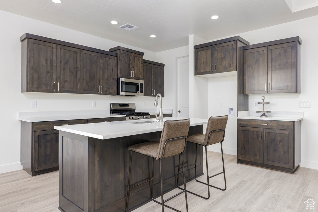 Kitchen with stainless steel appliances, light wood-style floors, baseboards, dark brown cabinets, and recessed lighting