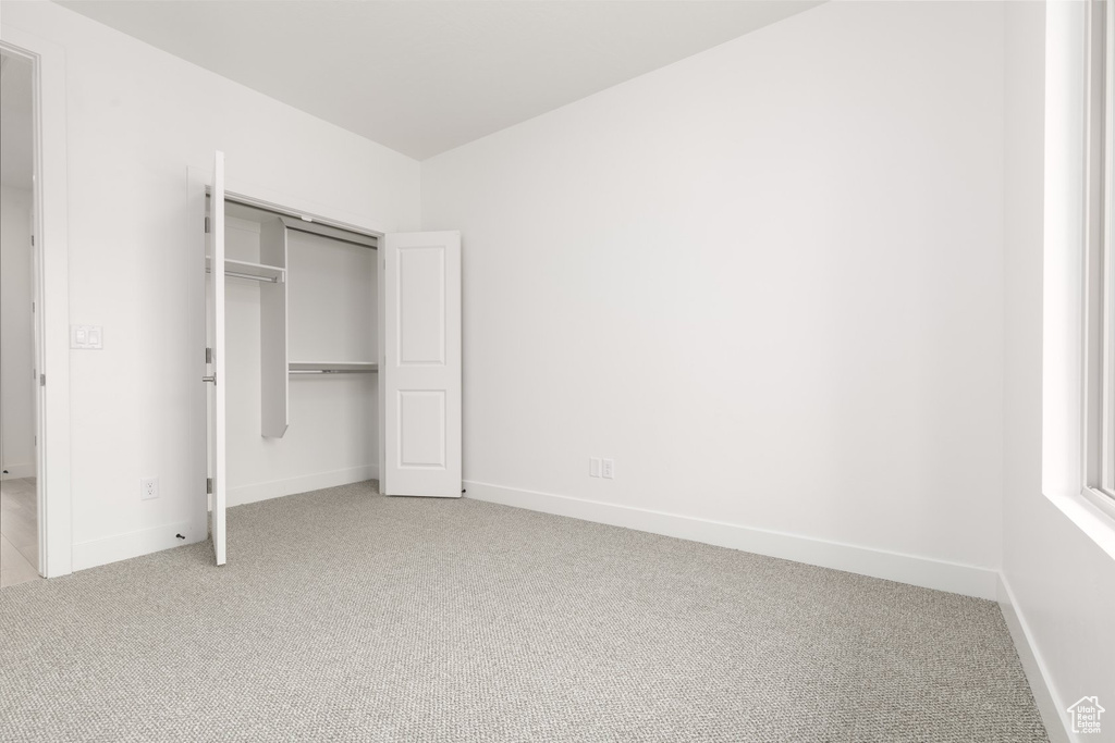 Unfurnished bedroom featuring light colored carpet, baseboards, and a closet