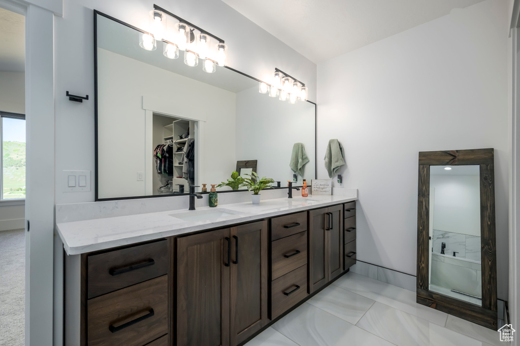 Bathroom featuring double vanity, marble look tiles, a walk in closet, and a shower