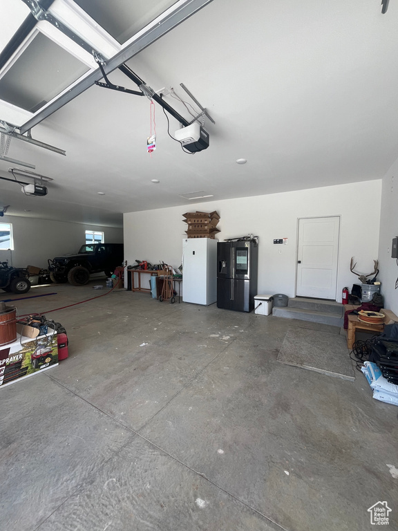 Garage featuring a garage door opener, fridge with ice dispenser, and freestanding refrigerator