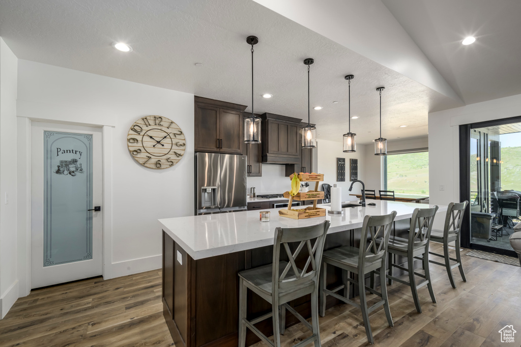 Kitchen with stainless steel refrigerator with ice dispenser, a spacious island, dark wood-style flooring, dark brown cabinetry, and light countertops
