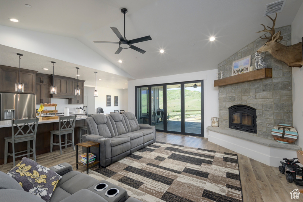 Living room featuring lofted ceiling, light wood finished floors, ceiling fan, a stone fireplace, and recessed lighting