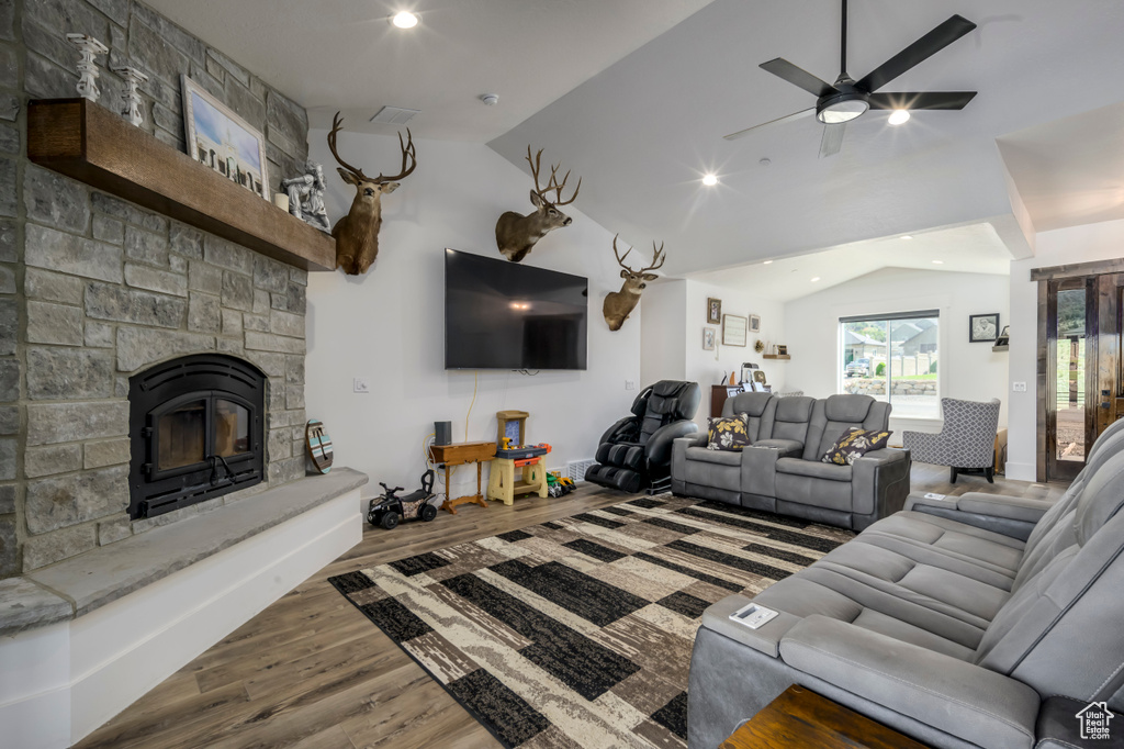 Living area with lofted ceiling, wood finished floors, a ceiling fan, a stone fireplace, and recessed lighting