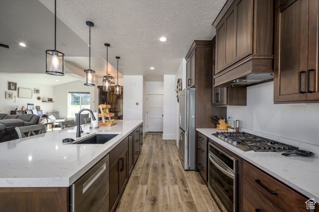 Kitchen featuring stainless steel appliances, a sink, open floor plan, light wood-type flooring, and a center island with sink