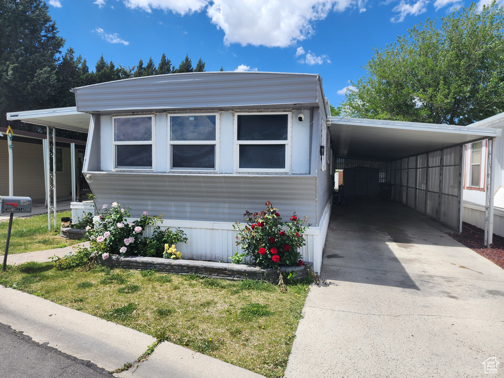 Manufactured / mobile home featuring concrete driveway, an attached carport, and a front yard