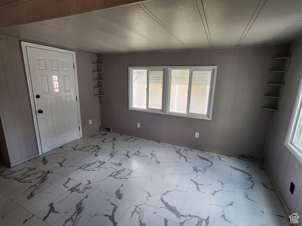 Foyer with healthy amount of natural light, light marble finish floors, baseboards, and wooden walls