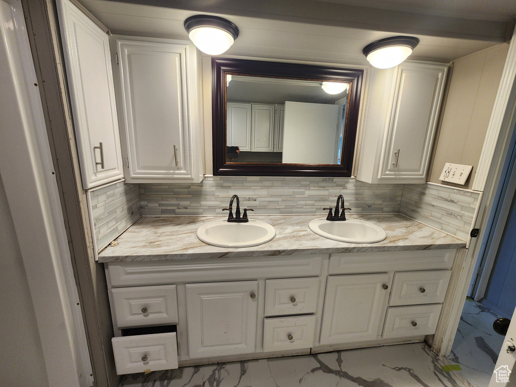 Bathroom with marble finish flooring, double vanity, and backsplash