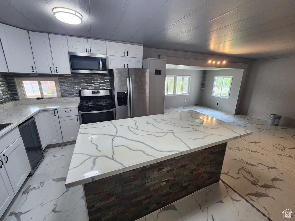 Kitchen with stainless steel appliances, light marble finish floors, light stone countertops, and white cabinetry