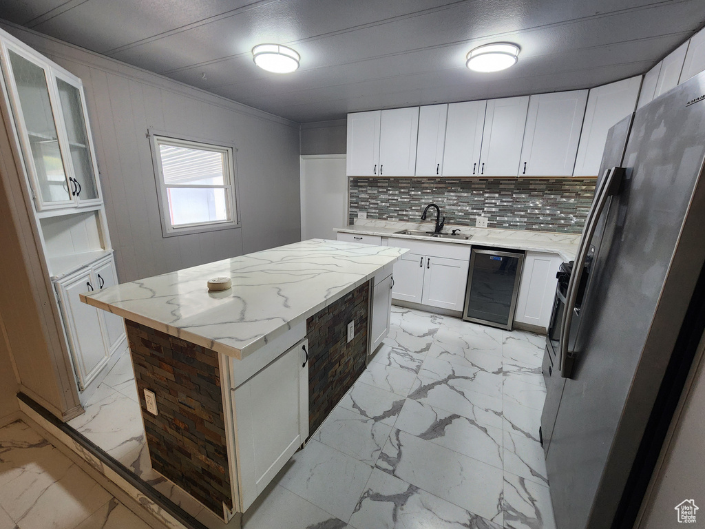 Kitchen featuring beverage cooler, light marble finish floors, stainless steel refrigerator with ice dispenser, a sink, and a kitchen island