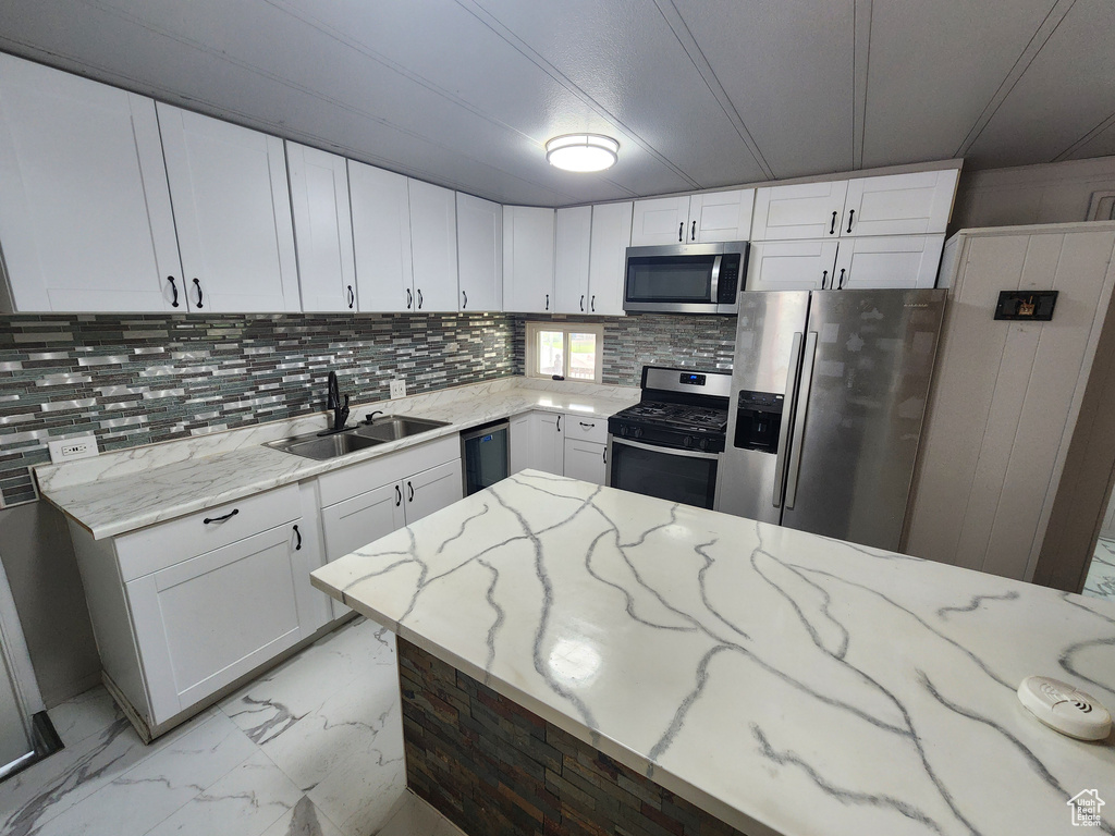 Kitchen featuring appliances with stainless steel finishes, a sink, light stone countertops, light marble finish floors, and white cabinetry