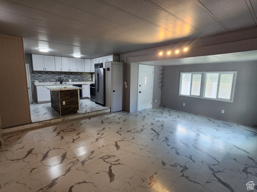 Kitchen featuring open floor plan, light countertops, a center island, light marble finish floors, and backsplash