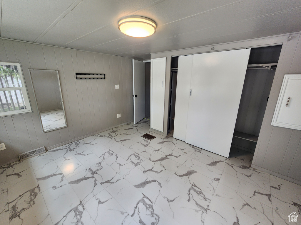 Unfurnished bedroom with light marble finish floors, wooden walls, and a closet