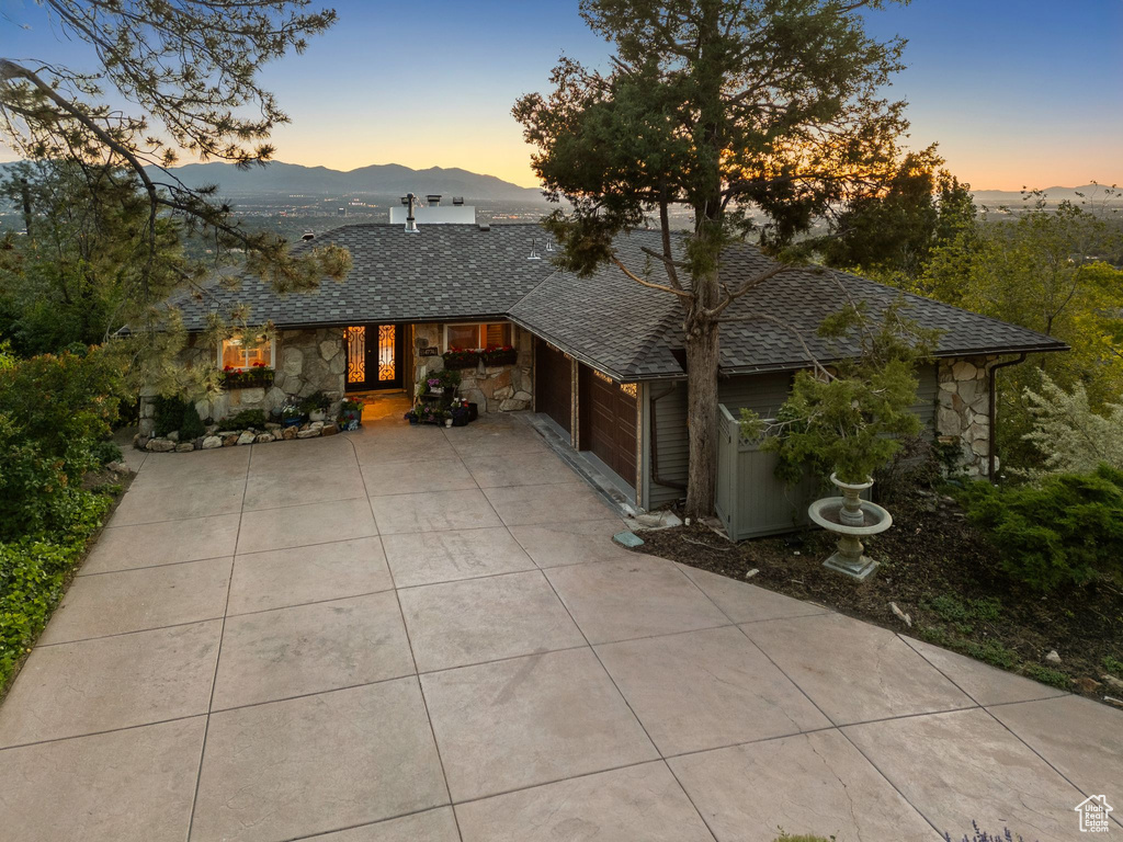 View of front facade with stone siding, driveway, a mountain view, an attached garage, and roof with shingles