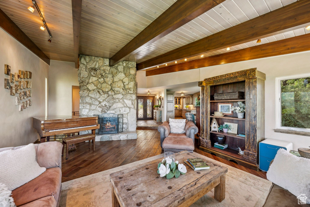 Living area featuring rail lighting, wood-type flooring, a fireplace, healthy amount of natural light, and wood ceiling with exposed beams