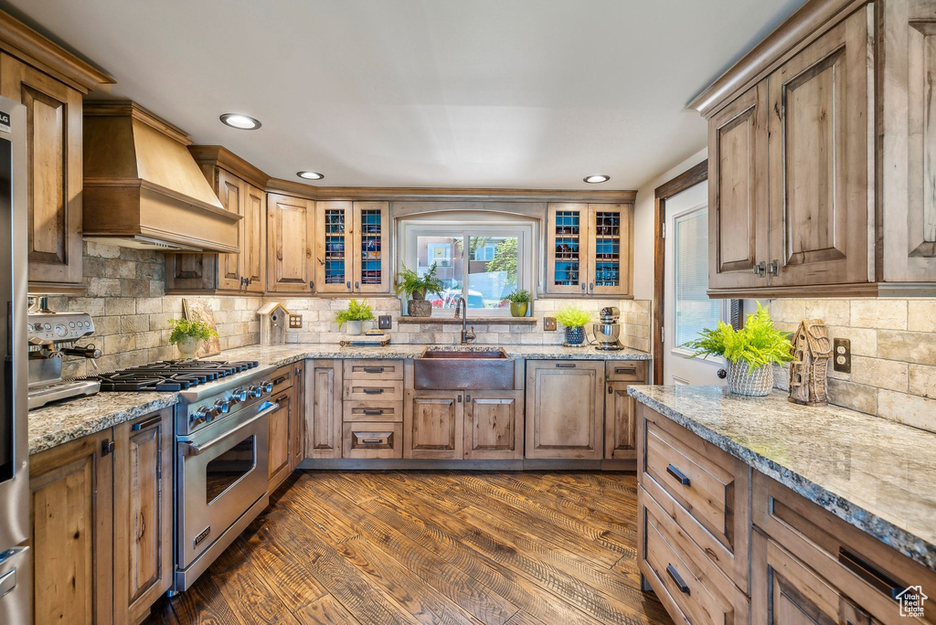 Kitchen featuring stainless steel range, a sink, custom range hood, tasteful backsplash, and light stone counters