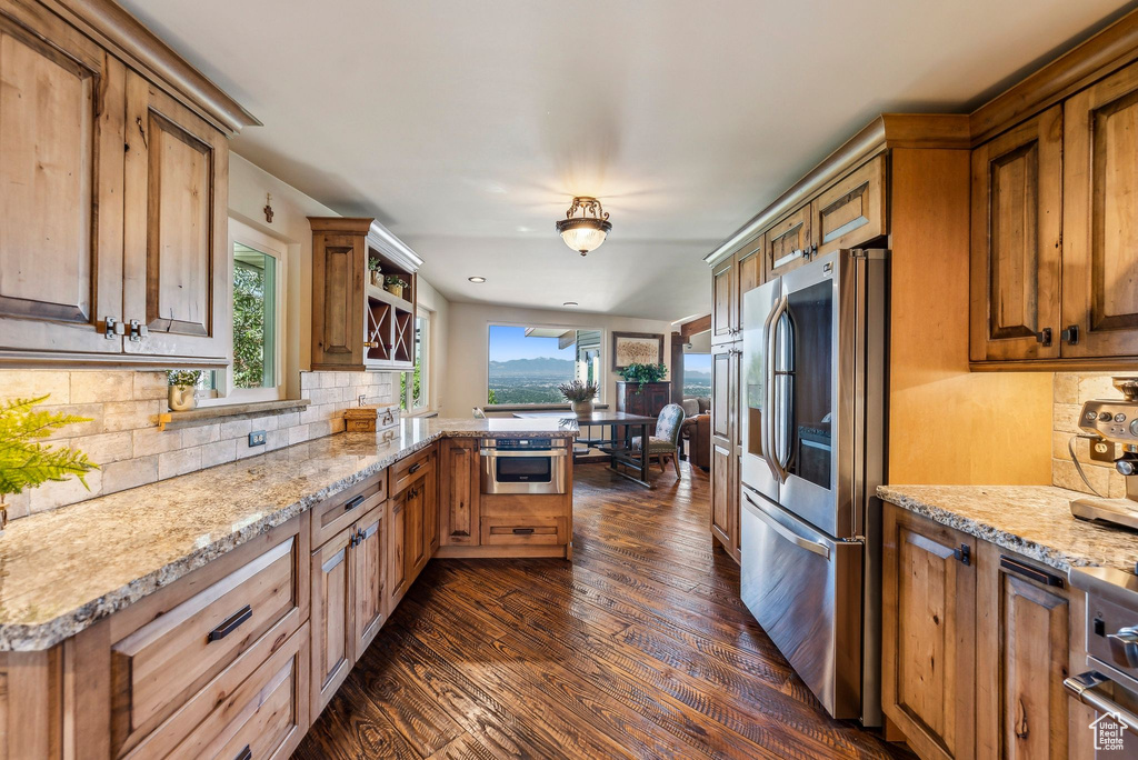 Kitchen featuring appliances with stainless steel finishes, dark wood finished floors, backsplash, a peninsula, and light stone countertops