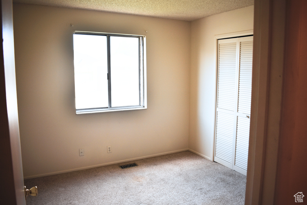 Unfurnished bedroom with carpet, multiple windows, a closet, baseboards, and a textured ceiling
