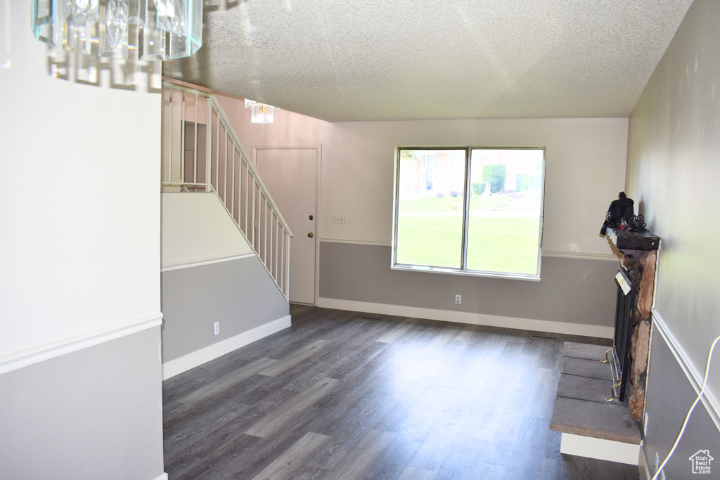 Unfurnished living room featuring a chandelier, stairway, wood finished floors, a textured ceiling, and baseboards