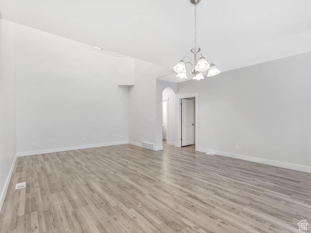 Empty room with light wood-type flooring, arched walkways, a chandelier, and baseboards