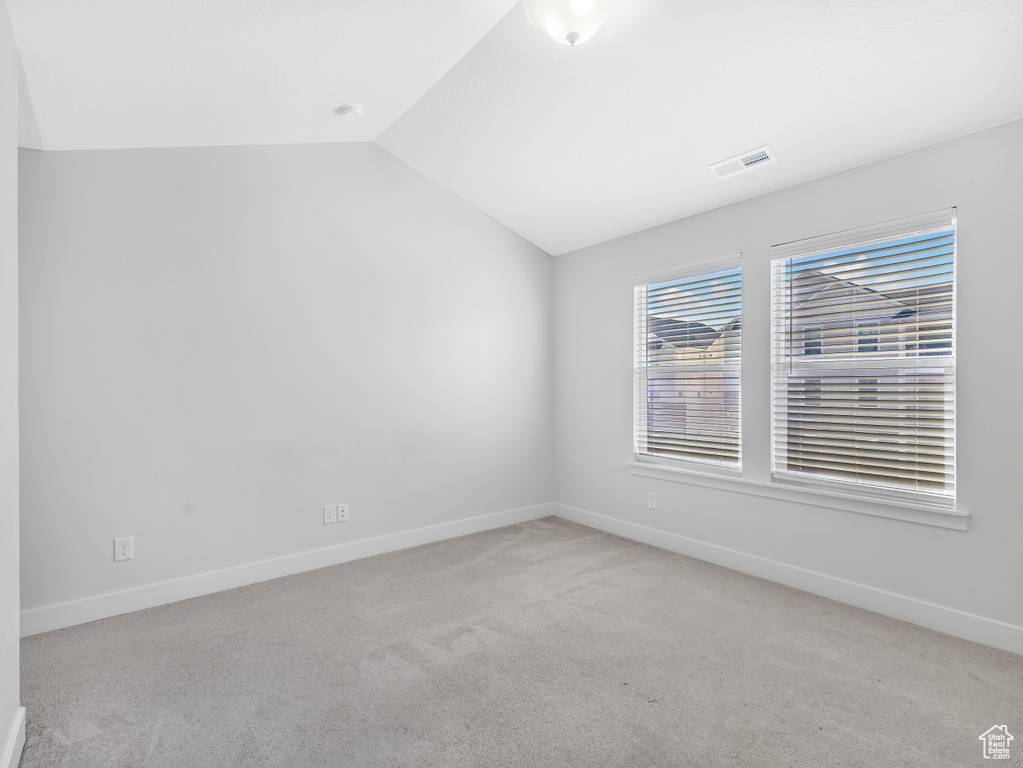 Empty room featuring light colored carpet, vaulted ceiling, and baseboards