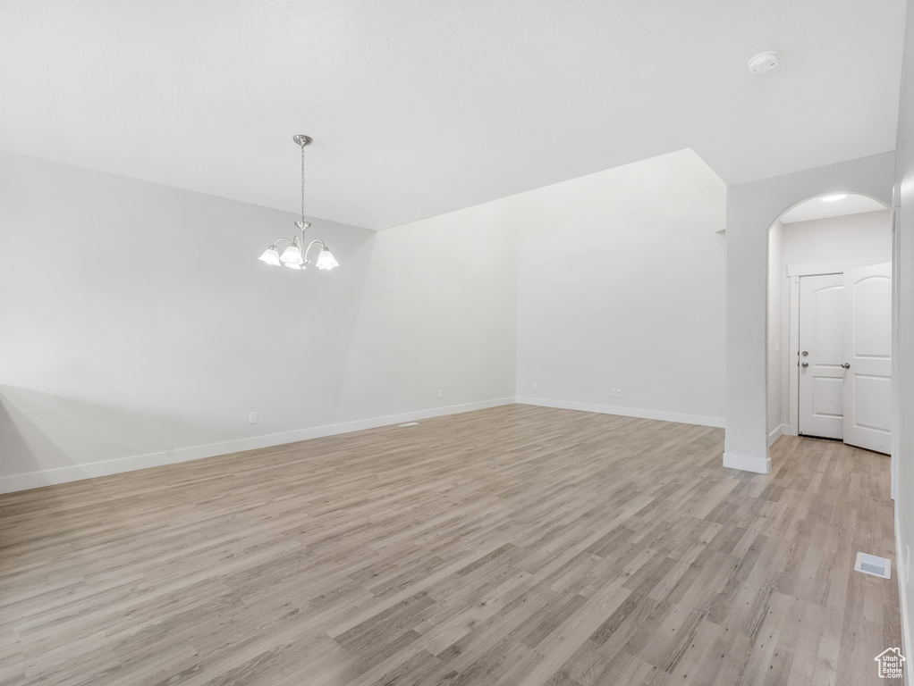 Spare room featuring light wood-style floors, baseboards, arched walkways, and a smoke detector