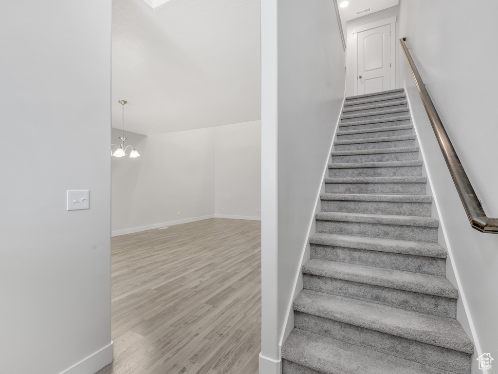 Stairway with wood finished floors, baseboards, and a chandelier