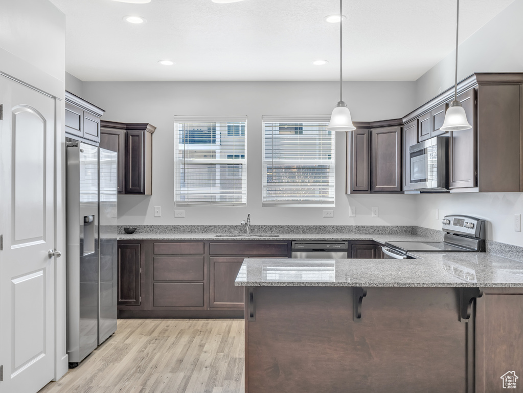 Kitchen with appliances with stainless steel finishes, a peninsula, dark brown cabinets, a sink, and recessed lighting