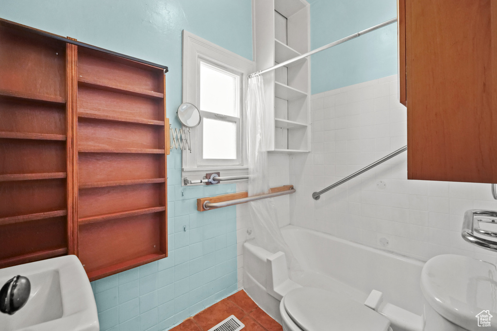 Full bathroom with tile walls, toilet, tile patterned floors, and shower / tub combo