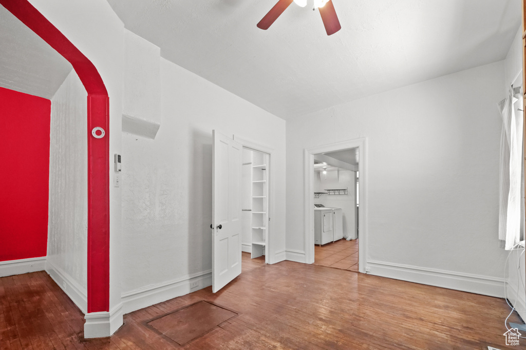 Empty room with a ceiling fan, wood finished floors, independent washer and dryer, arched walkways, and baseboards