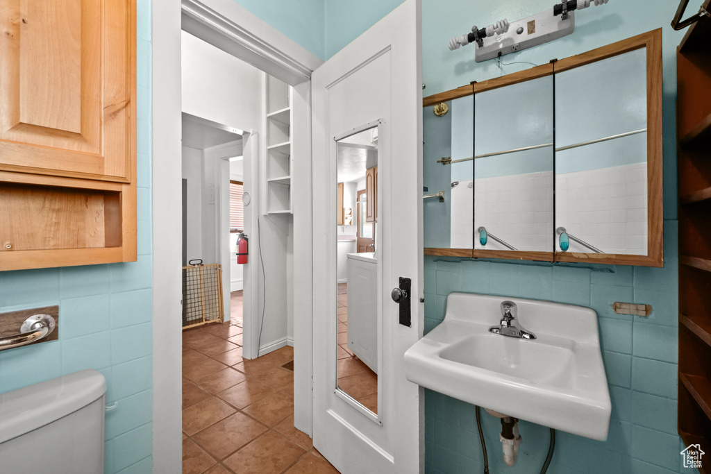 Bathroom featuring toilet, a sink, tile patterned flooring, and tile walls