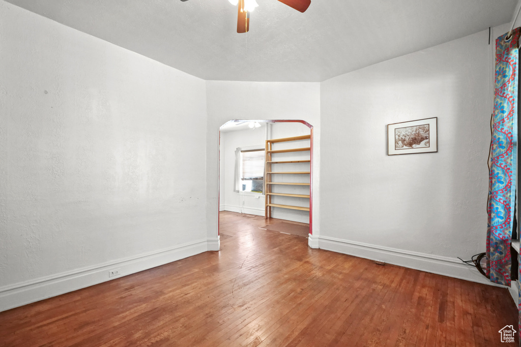 Spare room featuring a ceiling fan, hardwood / wood-style flooring, baseboards, and arched walkways