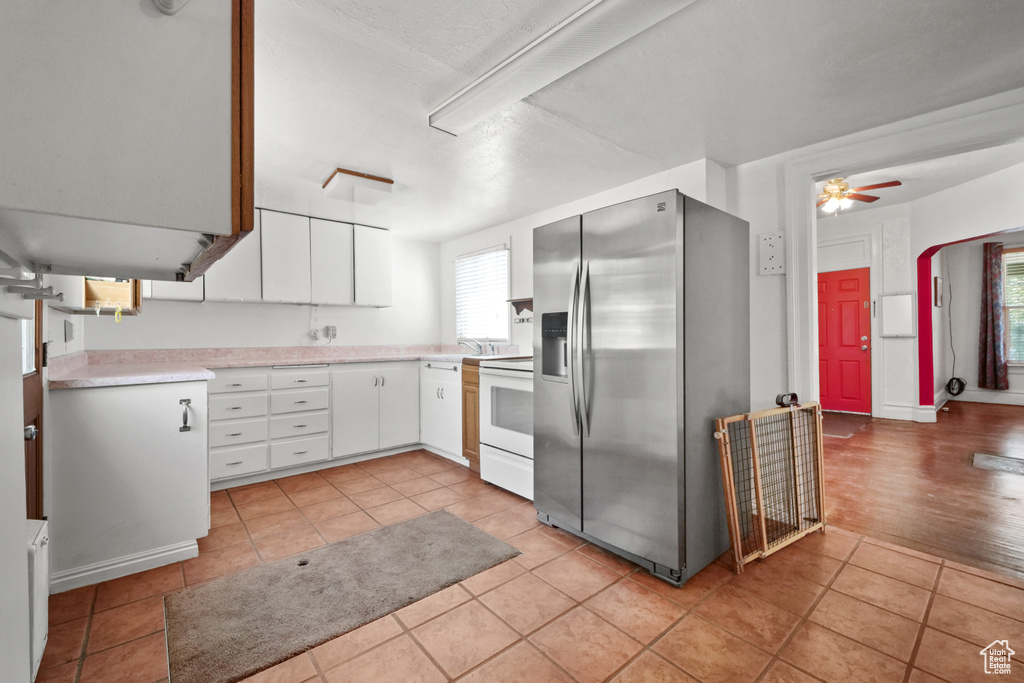 Kitchen featuring stainless steel refrigerator with ice dispenser, electric range, light tile patterned floors, light countertops, and white cabinetry