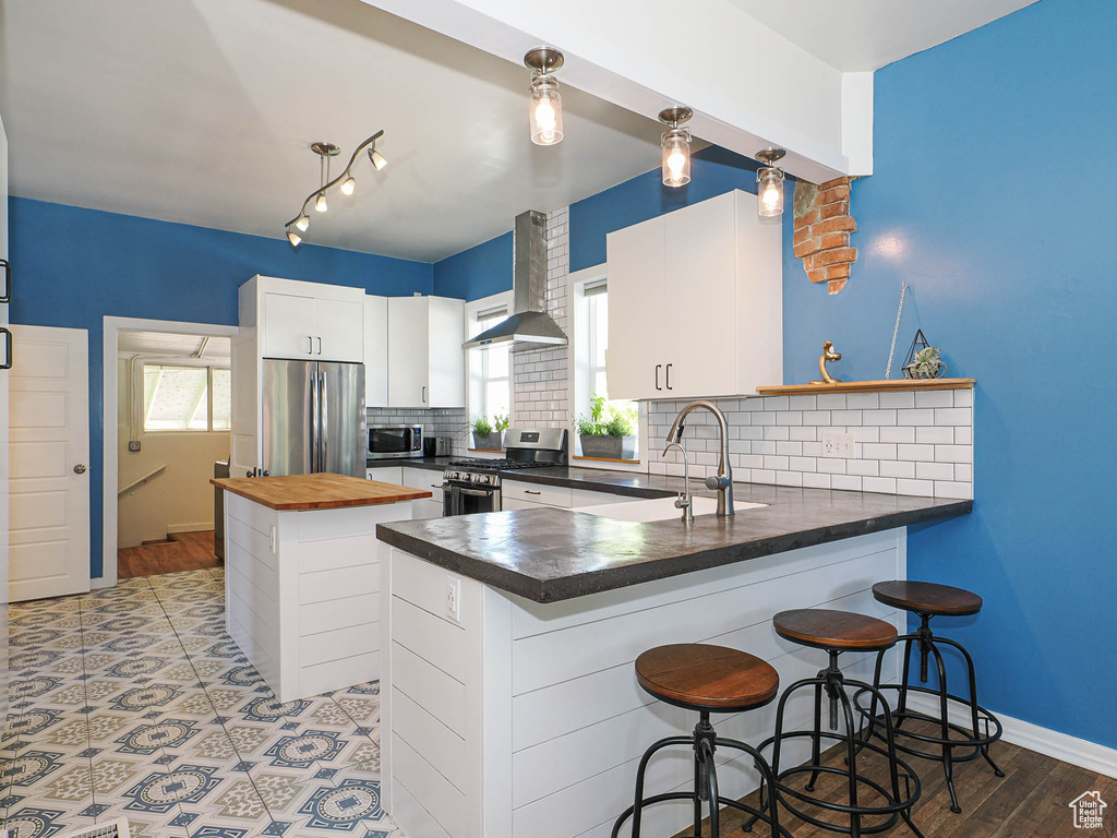 Kitchen featuring appliances with stainless steel finishes, wall chimney range hood, a sink, butcher block countertops, and backsplash