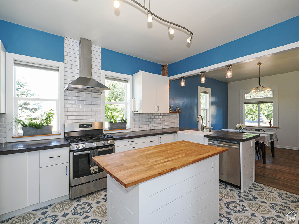 Kitchen with stainless steel appliances, wall chimney exhaust hood, a sink, a peninsula, and butcher block countertops