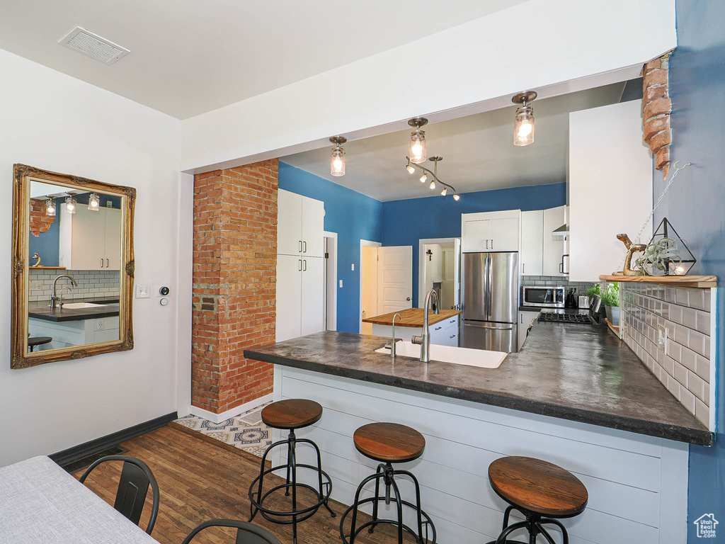 Kitchen featuring stainless steel appliances, a sink, a peninsula, dark countertops, and tasteful backsplash
