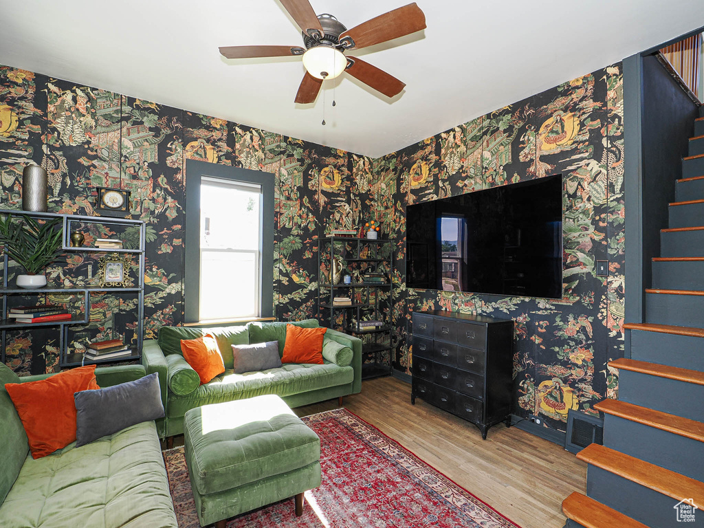 Living room featuring stairs, wallpapered walls, wood finished floors, and ceiling fan