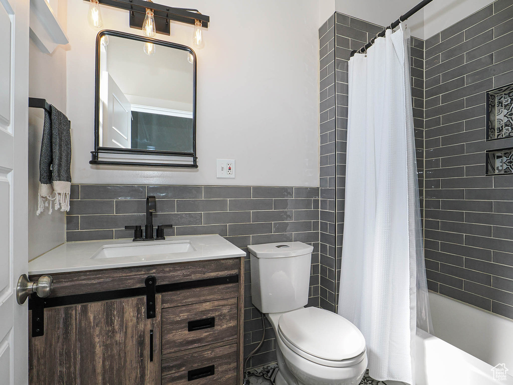 Full bath with vanity, toilet, tile walls, shower / tub combo with curtain, and a wainscoted wall