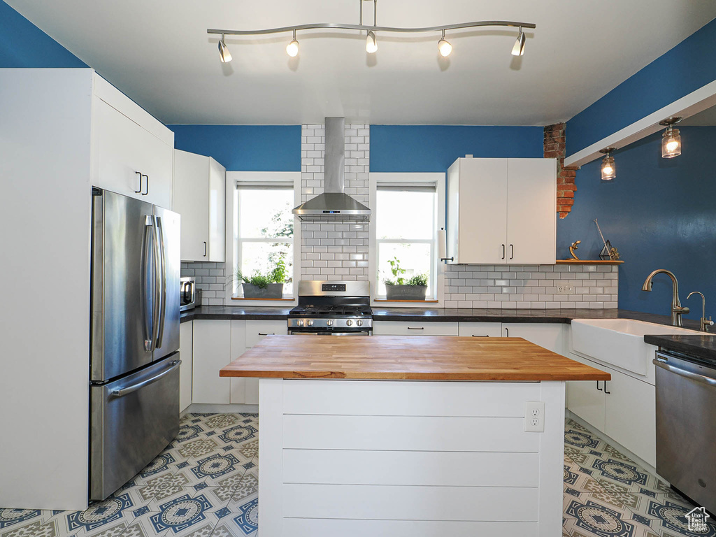 Kitchen featuring stainless steel appliances, wooden counters, wall chimney exhaust hood, and a sink