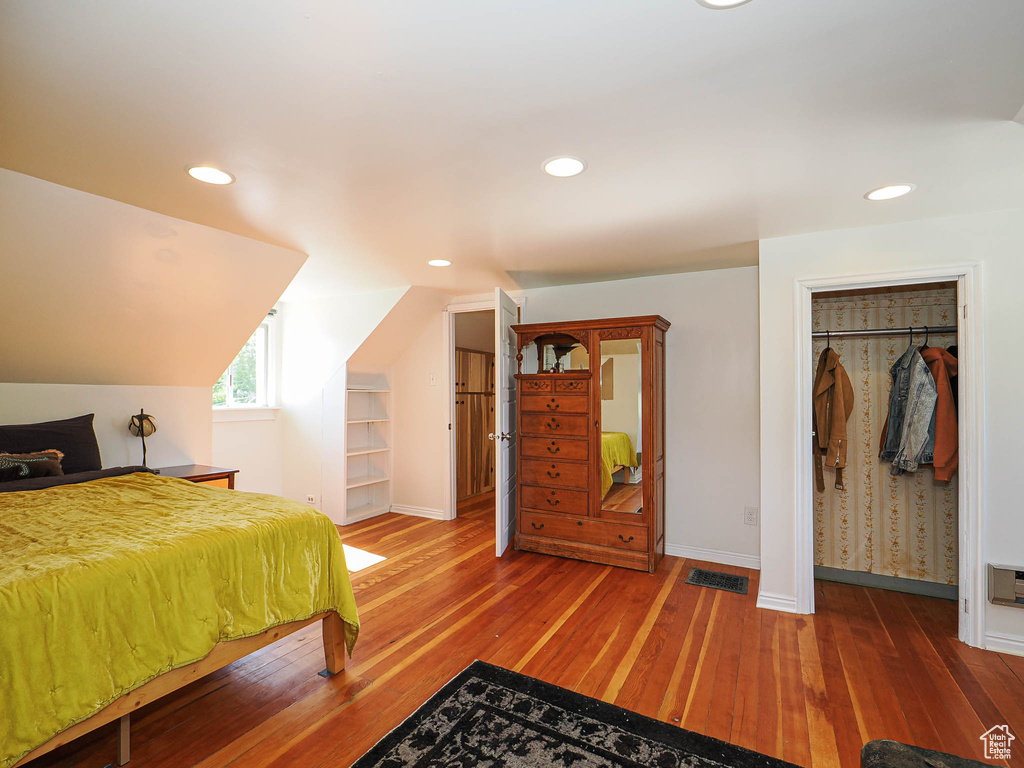 Bedroom with baseboards, wood-type flooring, recessed lighting, vaulted ceiling, and a walk in closet