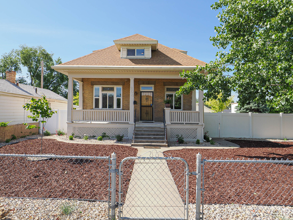 Bungalow featuring a gate, a porch, brick siding, and a fenced front yard