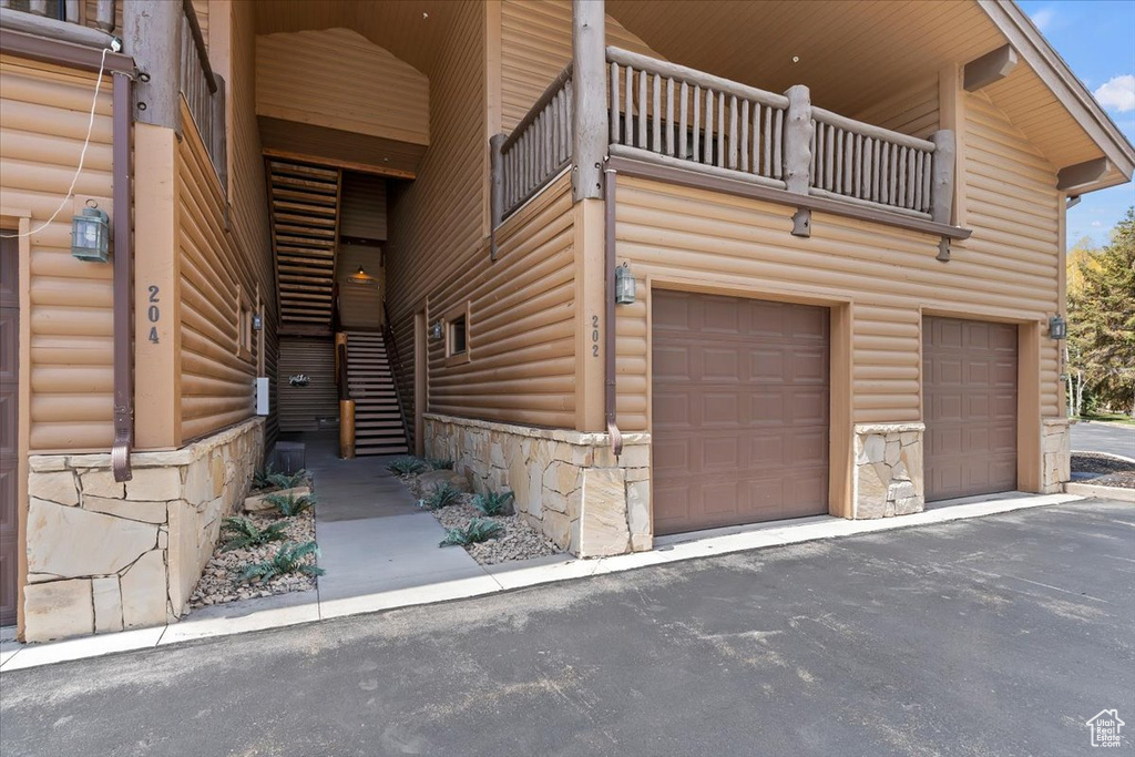 Exterior space with stone siding, an attached garage, a balcony, asphalt driveway, and faux log siding