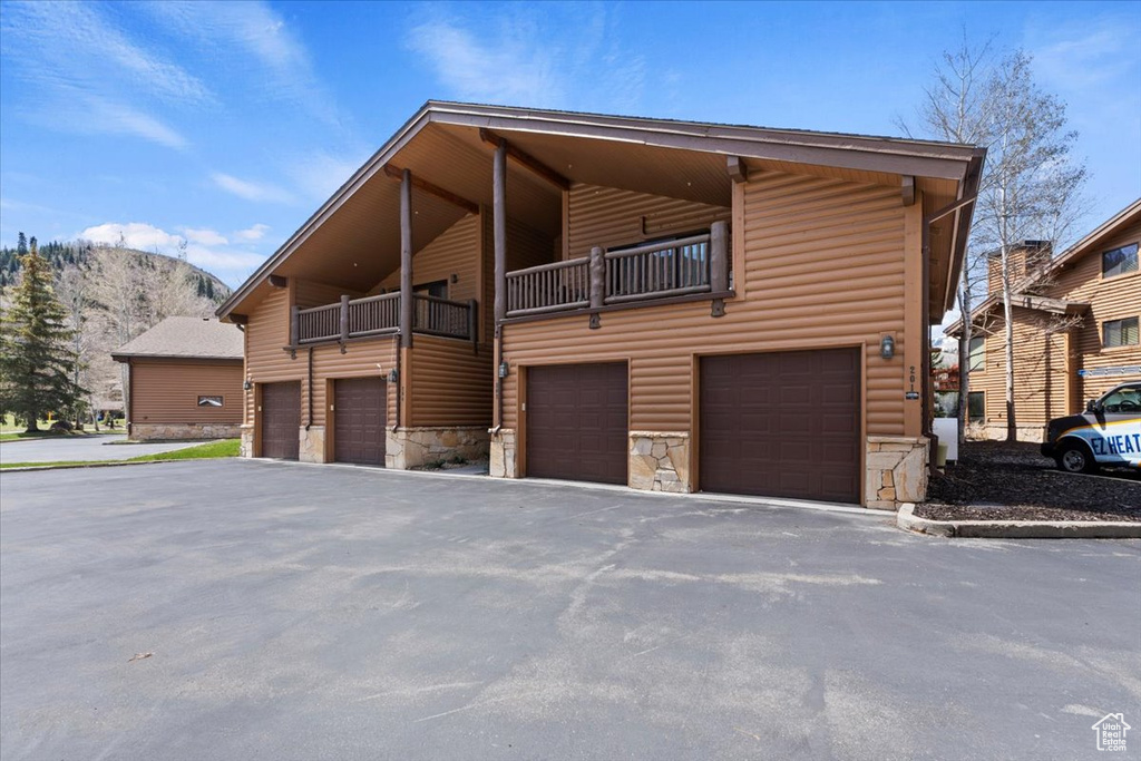 View of front of house with stone siding, log veneer siding, a garage, and driveway