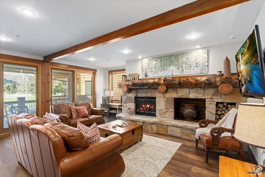 Living area featuring a stone fireplace, wood finished floors, beam ceiling, and recessed lighting