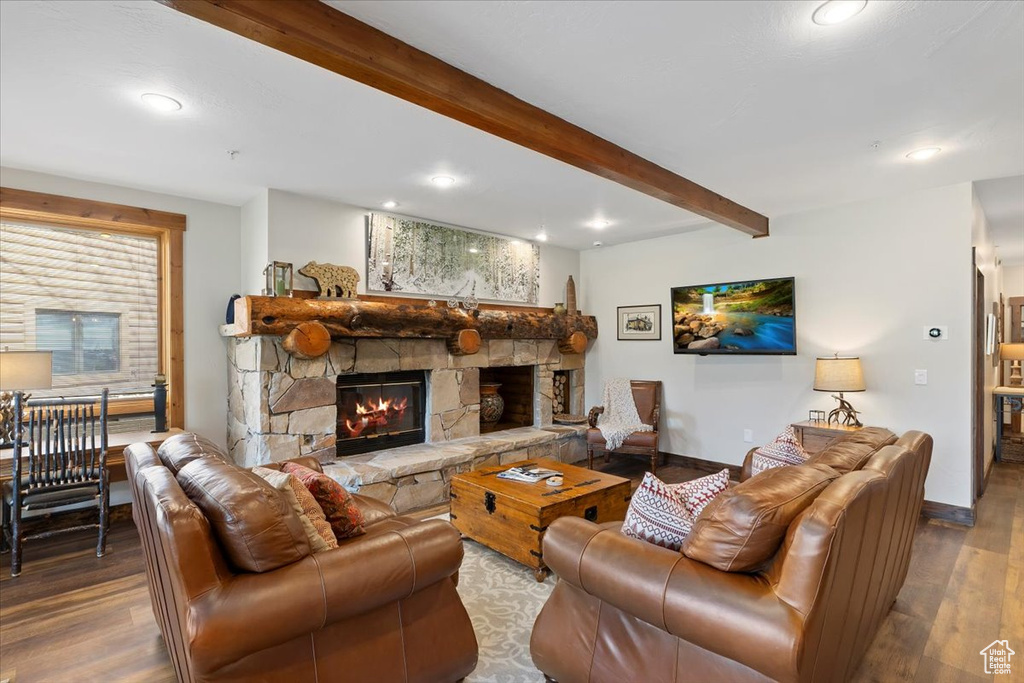 Living room featuring wood finished floors, beam ceiling, a stone fireplace, recessed lighting, and baseboards