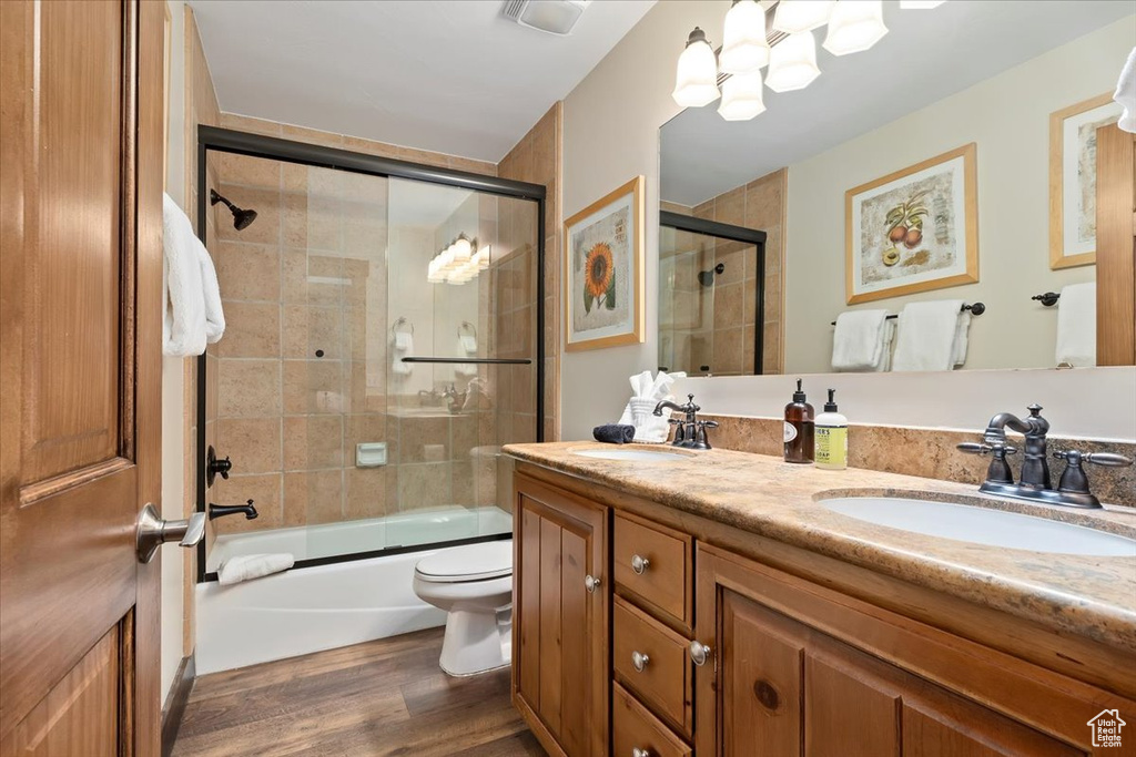 Bathroom with wood finished floors, enclosed tub / shower combo, double vanity, toilet, and a chandelier