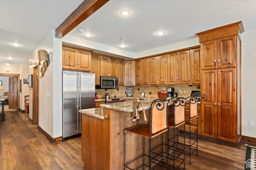 Kitchen with appliances with stainless steel finishes, dark wood-style floors, baseboards, backsplash, and a kitchen bar