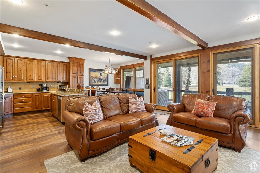 Living area with plenty of natural light, a chandelier, light wood-style flooring, beamed ceiling, and recessed lighting