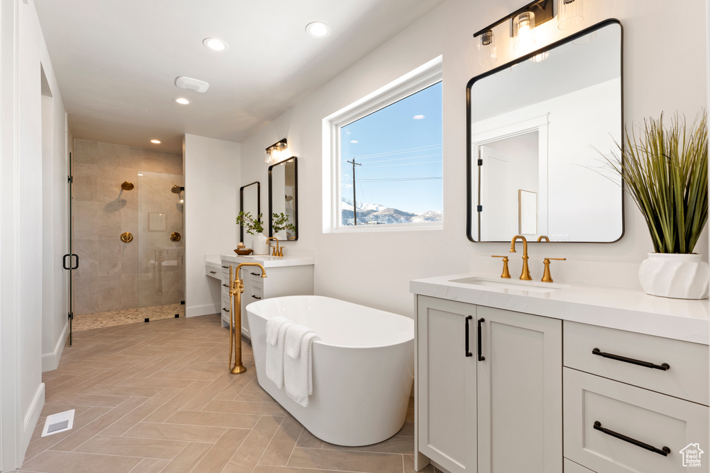 Bathroom with a shower stall, two vanities, a soaking tub, recessed lighting, and baseboards